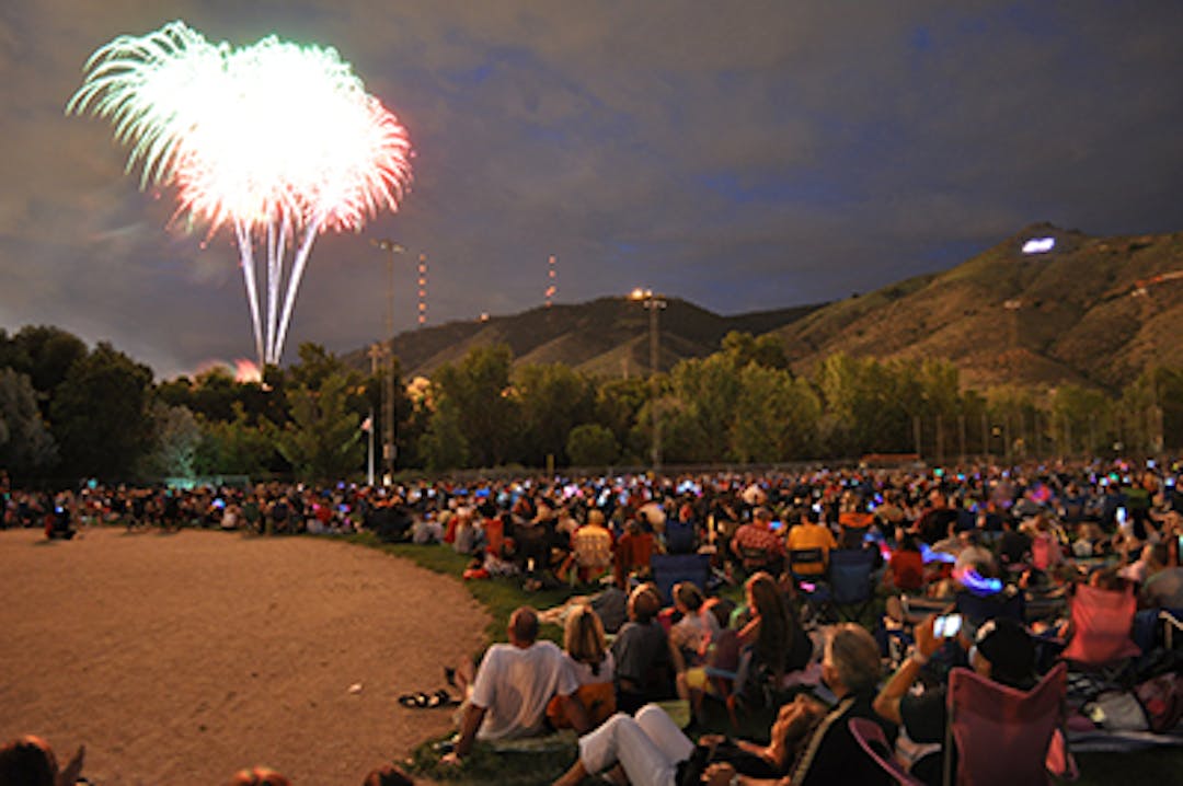 Crowds watch fireworks explode in the sky at night.