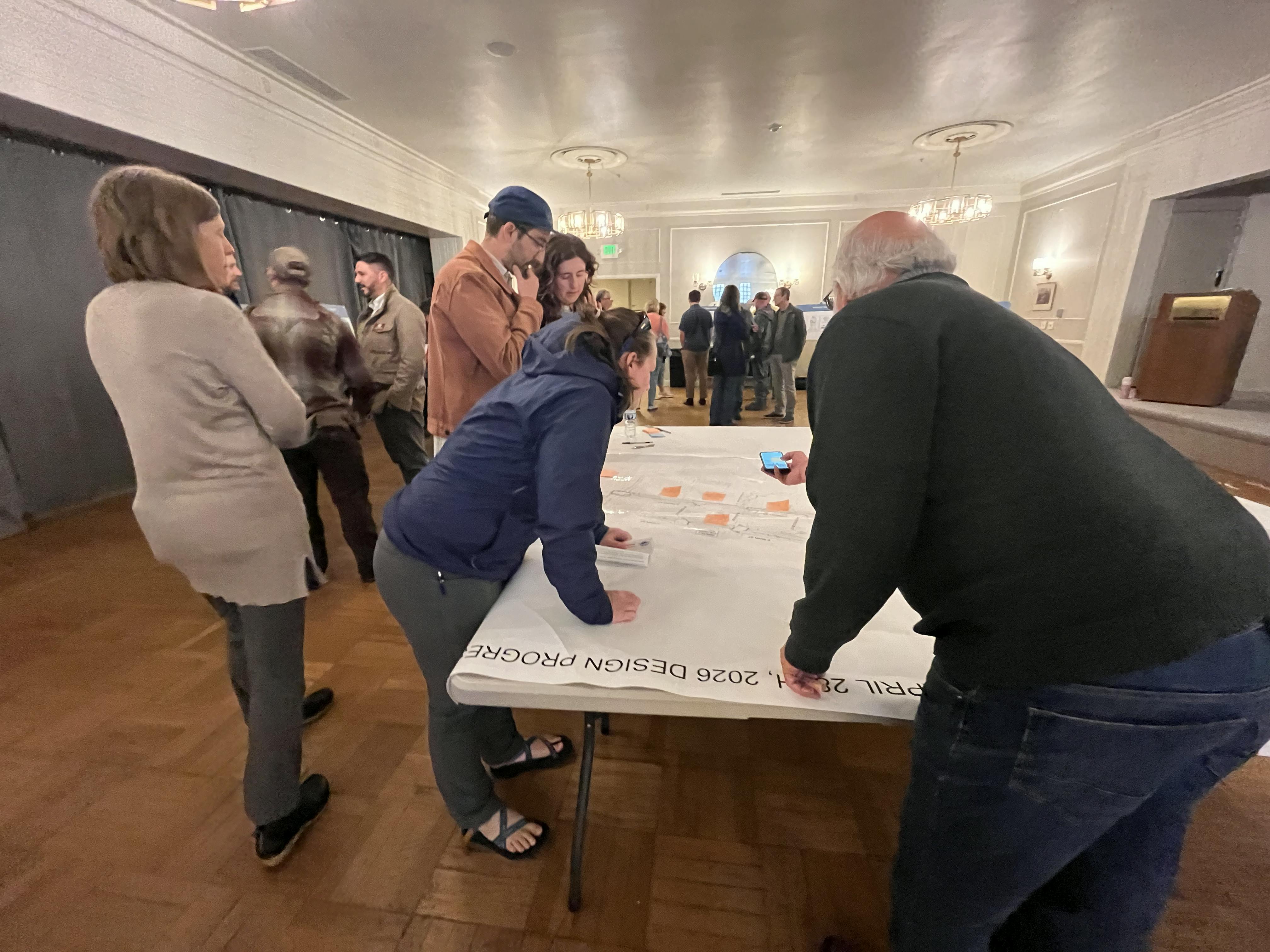 Open House 2 - Five people gather around a map at a table. One person is taking a picture with a phone..png