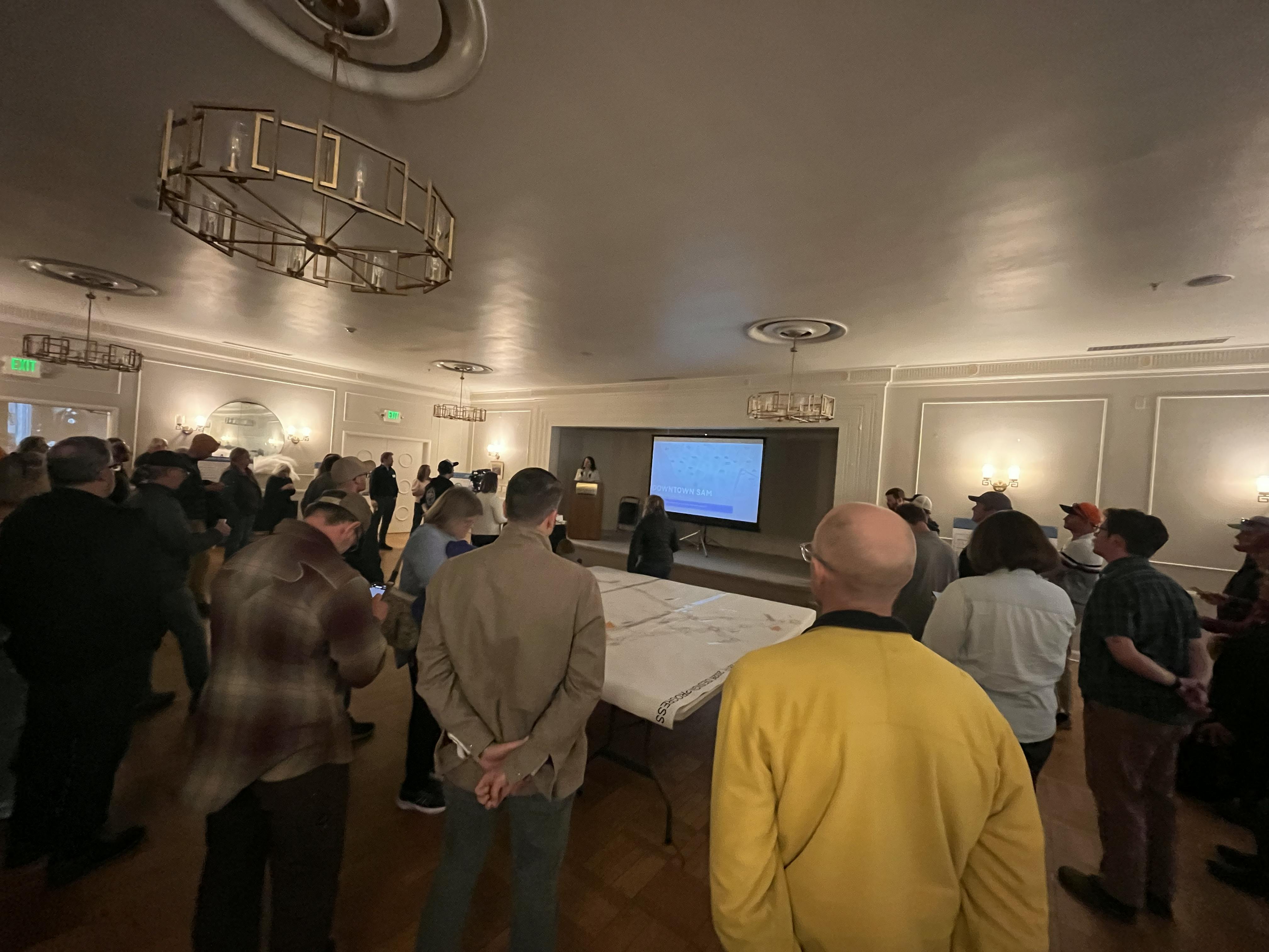 Open House 2 - People look at a projector screen while the mayor presents from a lectern.png