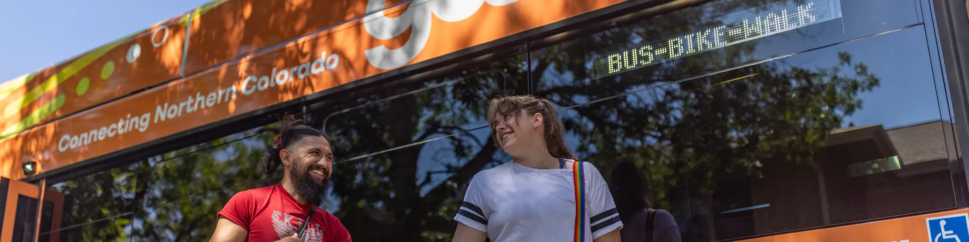 Man and woman smiling at each other in front of newly branded Gallop bus that reads "connecting Northern Colorado"