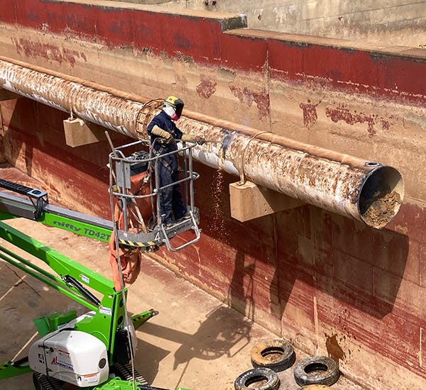 A crew member uses a blow torch to cut a section of a large water pipe.