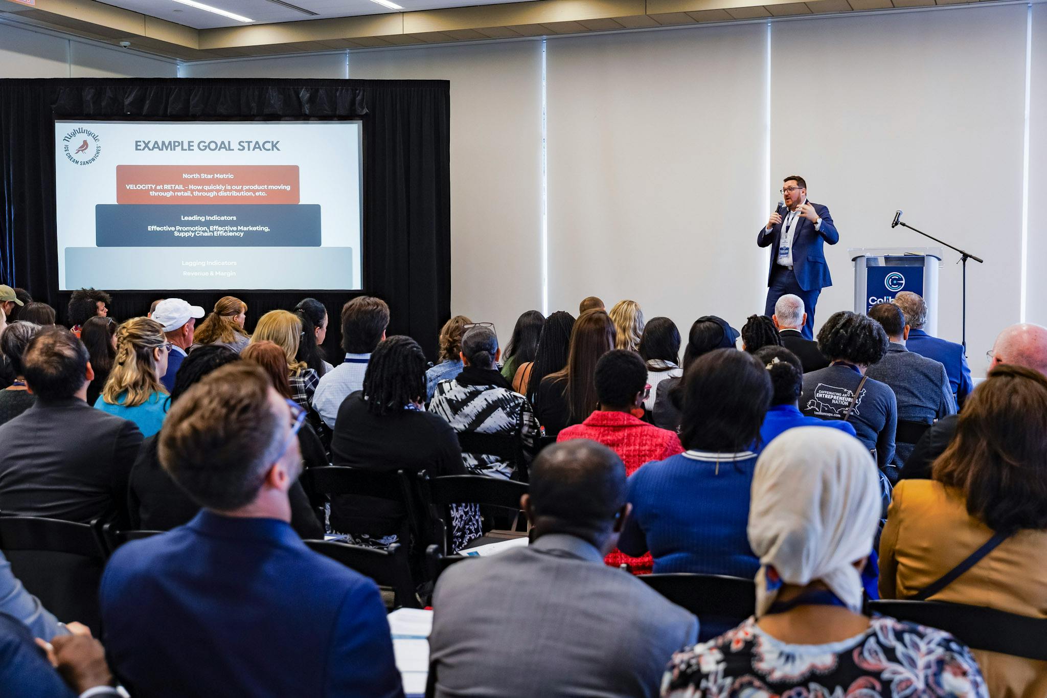 Presentation at the 2026 Calibrate Conference with speaker holding microphone and talking to the audience