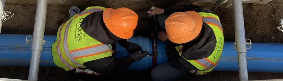 workers sit across a water main pipeline they are connecting together.