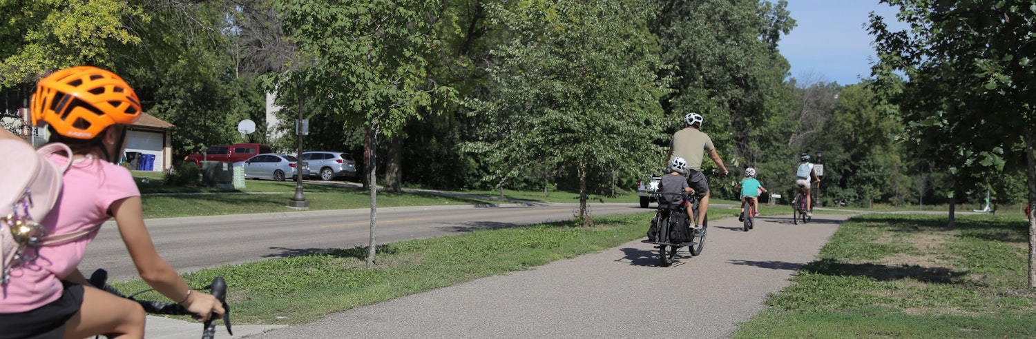 Family of three kids and their parents bike on a Saint Paul dedicated bike trail