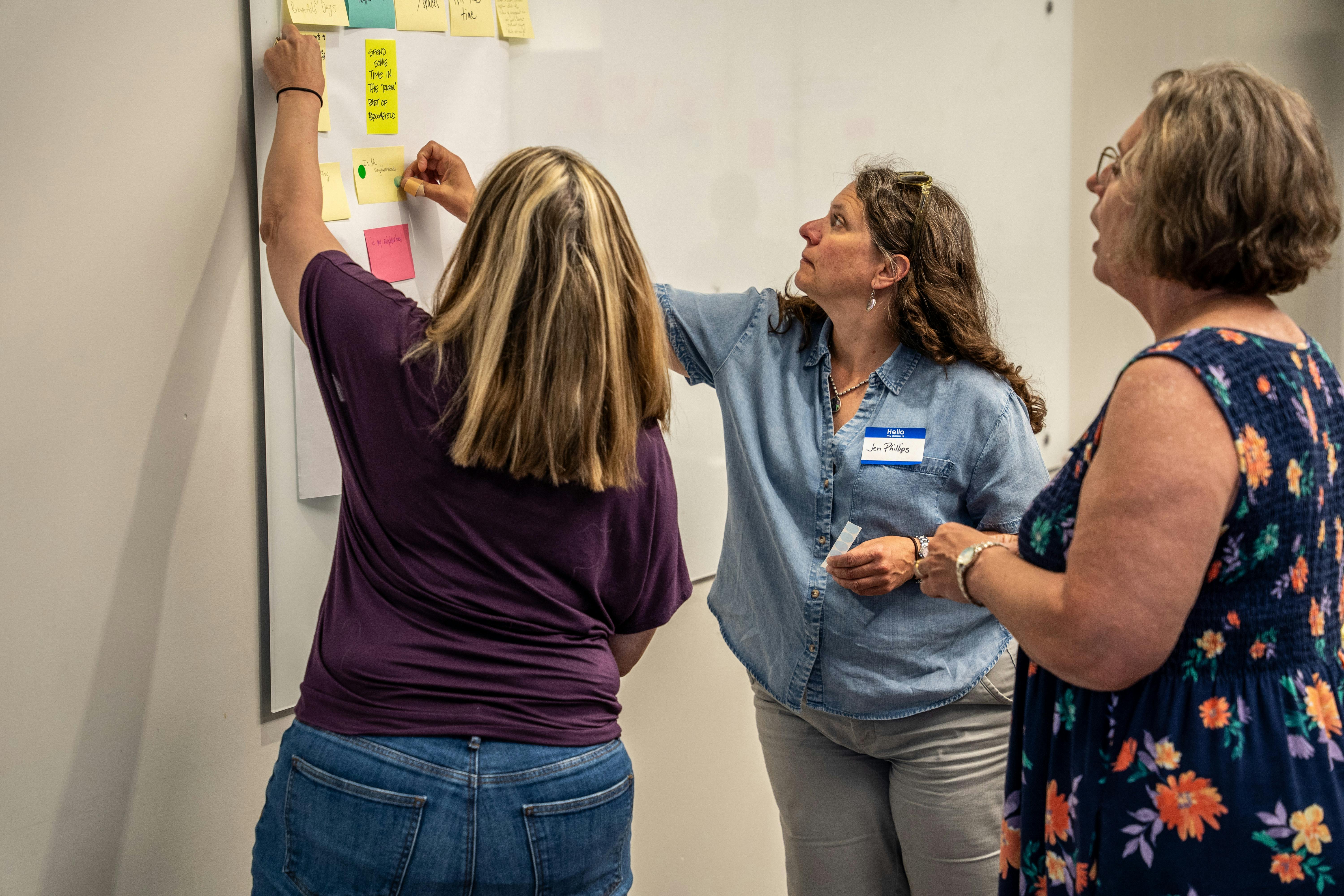 Three participants place their sticky notes on a poster