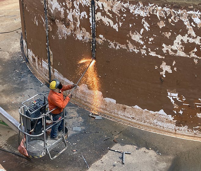 A crew member uses a blow torch to make cuts on the clarifier in secondary basin 2.