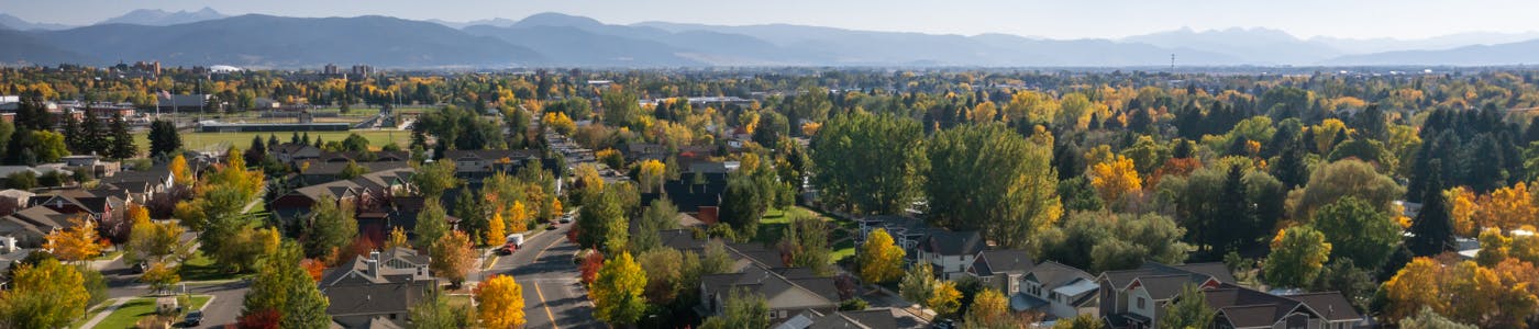 Arial view of Bozeman of a neighborhood with green and yellow trees, with blue mountains in the background,