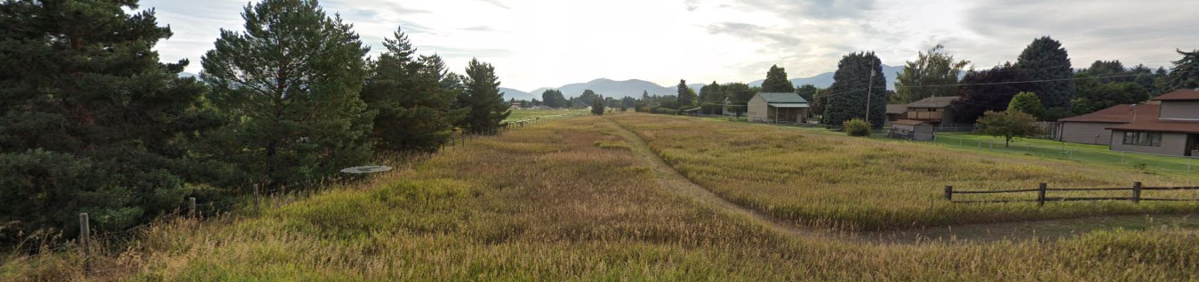 View of Rosecrest County Park on summer evening with green grasses and vehicle tracks into park