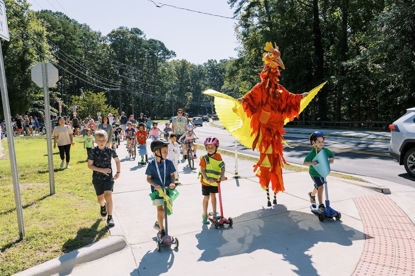A person in a paper bird costume walks with kids on a multiuse path 