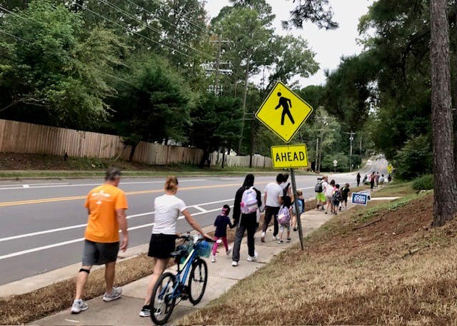 Kids walking and biking on a sidewalk with a school sign nearby