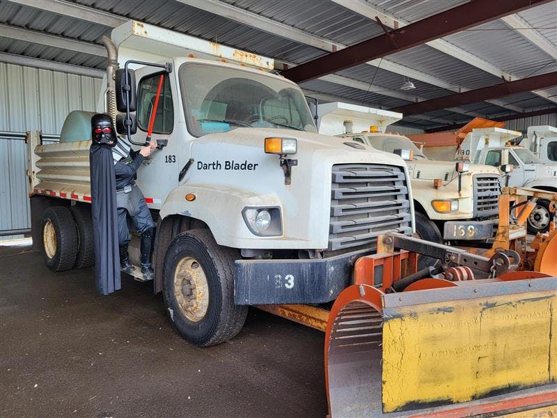 Image of man dress in Darth Vader Costume standing on a snowplow named "Darth Blader."