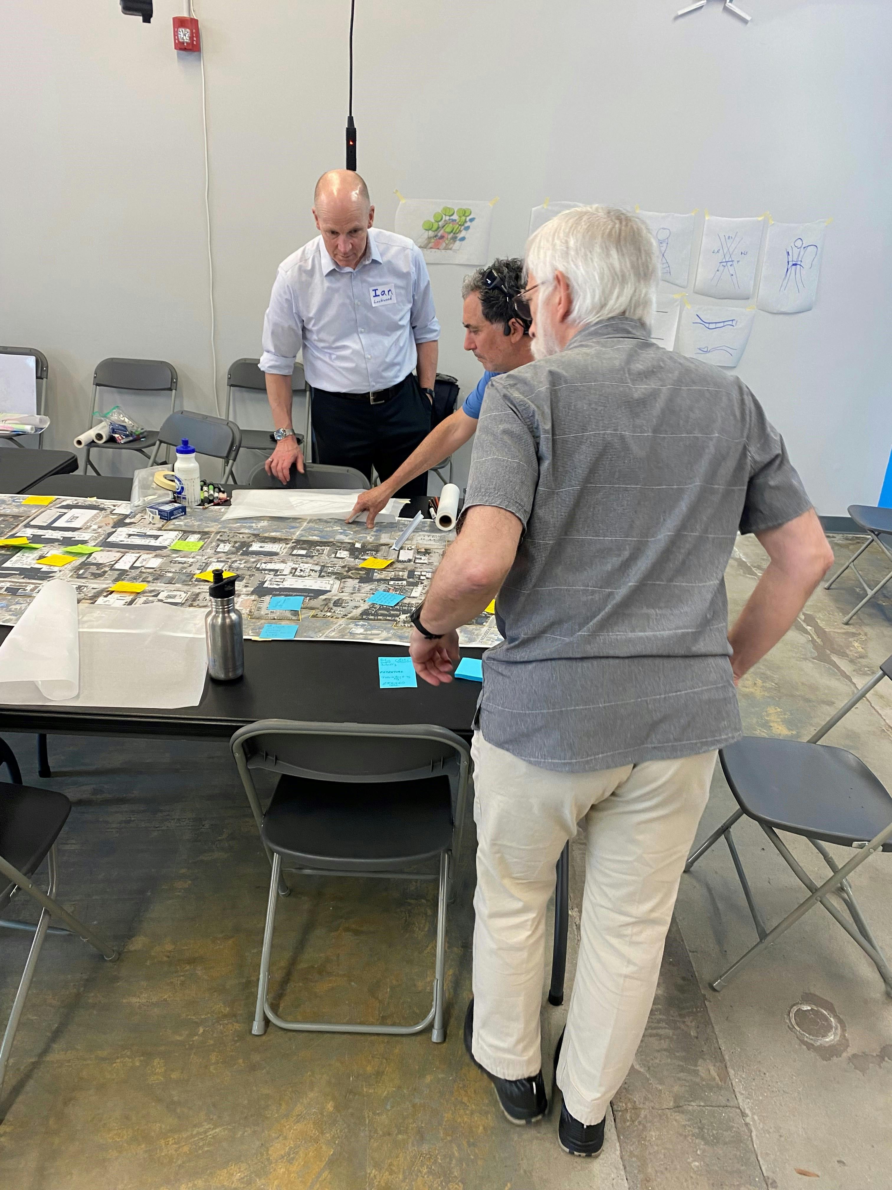 Two community members point to areas on a map of Downtown Chapel Hill out to a project team member 