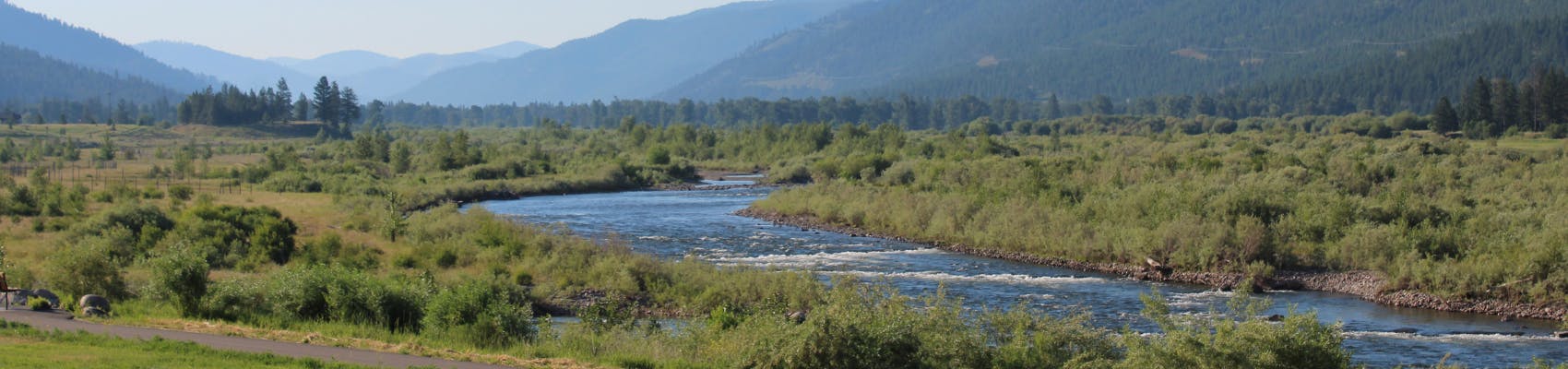 Milltown Confluence area with river, greenery and mountains in the background on sunny summer day