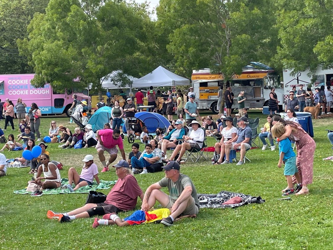 People sitting on the lawn at Cromwell Park during Celebrate Shoreline 2024 listening to music.